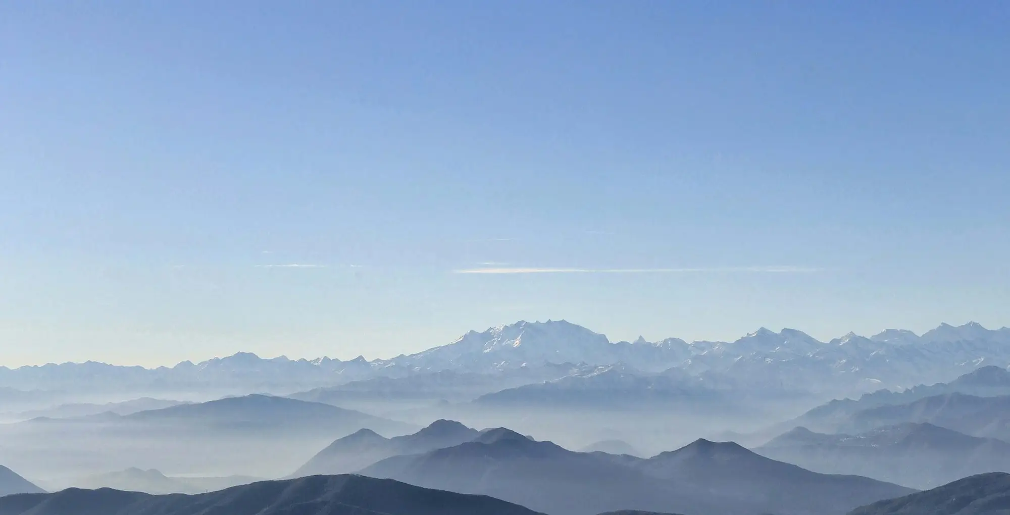 Ridges receding into haze above the Mendrisiotto, seen from Monte Generoso, with the snow line of the high Alps on the horizon.